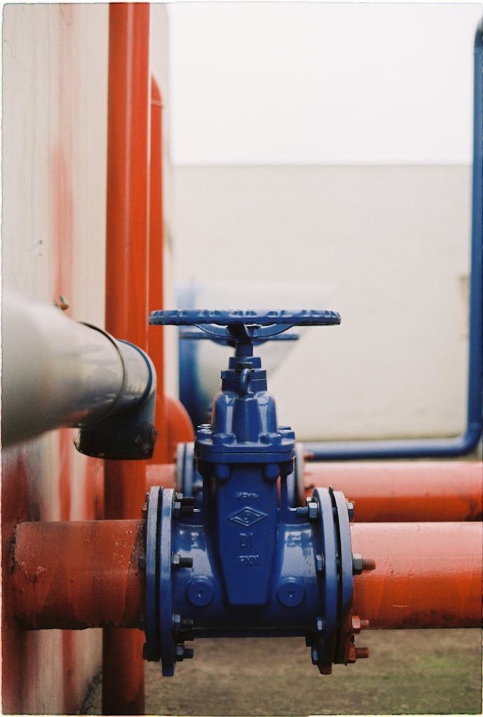 Close-up of a blue gate valve on red pipes, showcasing industrial plumbing.